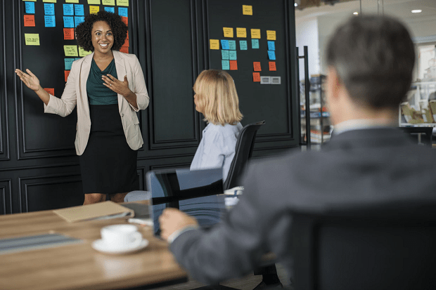 Someone in an office explaining something, with a wall full of post-it notes behind them