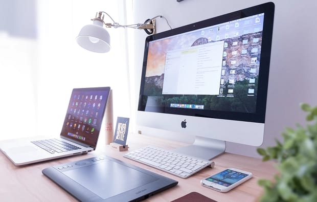 Several different computers and mobiles devices lined up on a desk