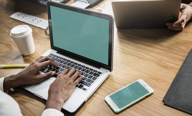 A couple of people working on laptops at a desk, with a phone set next to one of them